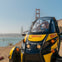 A person sits in a yellow and black GoCar with the Golden Gate Bridge visible in the background on a sunny day.