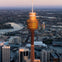 Elevated view of a city featuring a tall observation tower with a golden hue at sunset, surrounded by buildings and water.