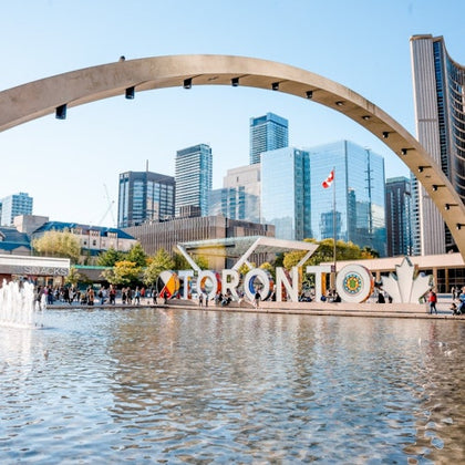 Nathan Phillips Square in Toronto featuring a fountain, the "Toronto" sign, and modern buildings under a clear sky.