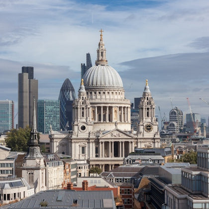 View of St. Paul's Cathedral in London, with modern skyscrapers and urban buildings in the background under a cloudy sky.