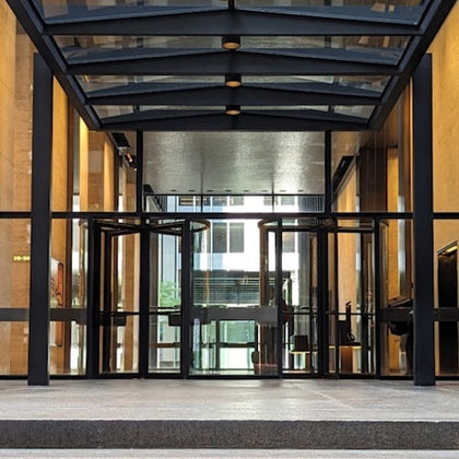 A modern glass entryway with revolving doors and a transparent canopy, leading into a building interior.