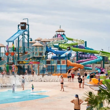 A water park with colorful slides, structures, and people enjoying pools and fountains under a cloudy sky.