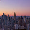 A cityscape at sunset featuring the Empire State Building and surrounding skyscrapers under a colorful sky.