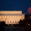 The Lincoln Memorial illuminated at night with a large red moon rising in the background.