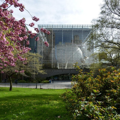 A glass building with a large sphere inside, surrounded by greenery and blooming trees on a sunny day.