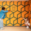Two individuals interact with a perspective illusion wall at the Museum of Illusions in Denver, featuring a geometric pattern.
