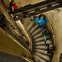 Several people descend a spiral staircase in an industrial setting with metal steps and a concrete wall.