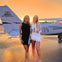 Two women in stylish outfits stand in front of a small airplane at sunset, with "Sky Tours Miami" visible on the plane's tail.