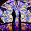 Two silhouetted figures standing inside a brightly lit, kaleidoscope-patterned room with reflective flooring.