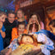 Six people gathered around a person dressed as Sleeping Beauty, who is lying on a rustic bed. A "Bakery" sign is visible behind them.