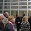 A group of people outside a modern building, with one man pointing upwards while speaking to the others.