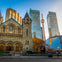 A historic stone church with arched doors and windows stands in front of modern skyscrapers, including a tower with a CN Tower.