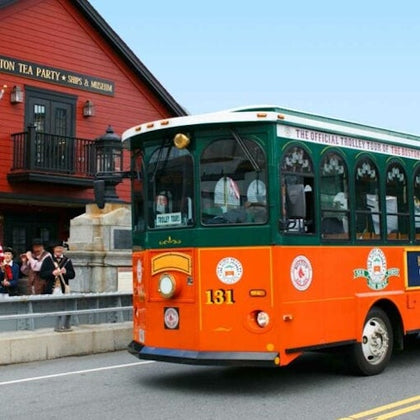 An orange and green trolley bus on a street near a red building labeled "Boston Tea Party Ships & Museum."