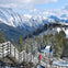 Snow-covered mountain view with a wooden stairway leading to a distant building with a Canadian flag. People wearing winter clothing.
