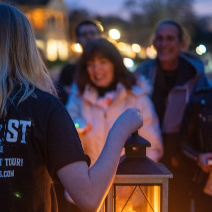 A tour guide holding a lantern while guests gather around to hear ghost stories
