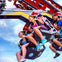 People riding a thrill ride at an amusement park, smiling and enjoying the experience with a blue sky background.