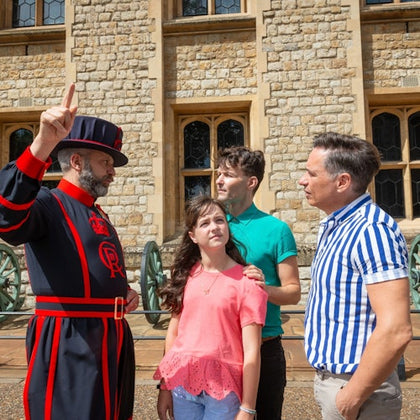 A uniformed guard gestures while speaking to a family of three outside a stone building with arched windows.