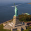 Aerial view of the Statue of Liberty on Liberty Island, with surrounding water and a boat streaming past.