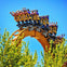 A group of friends laughing and hugging at an amusement park, with a roller coaster and American flags in the background.
