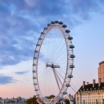 A large Ferris wheel against a partly cloudy sky with nearby buildings and a cityscape visible below.