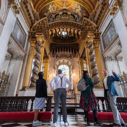 A group of four people stand and observe the ornate interior of a grand hall with intricate arches and golden decor.