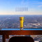 A tall glass of yellow drink on a table with a cityscape view through a large window, labeled 'CloudBar at 360 Chicago.'