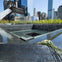 Memorial water fountain with names inscribed, surrounded by skyscrapers. Pink and white flowers are placed on the edge.