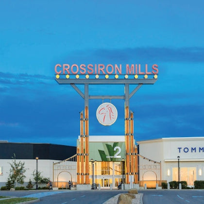 CrossIron Mills shopping center entrance with a large sign and surrounding shops, including Tommy Hilfiger under a twilight sky.