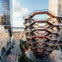 Modern, honeycomb-like structure surrounded by tall buildings, overlooking a waterfront and train tracks in an urban setting.
