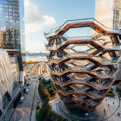 Modern, honeycomb-like structure surrounded by tall buildings, overlooking a waterfront and train tracks in an urban setting.