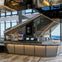 A modern cafe counter with beverage dispensers, menu screens, and a geometric backdrop, located in a high-rise setting.
