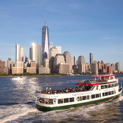A sightseeing cruise boat on the water with a group of people on board, with the New York City skyline in the background.