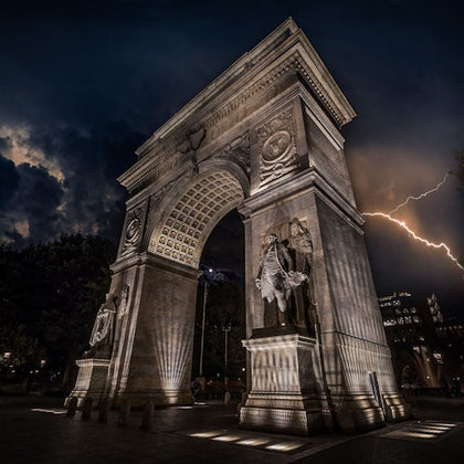Nighttime photo of the Washington Square Park in New York with lightning striking the sky