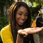 A woman smiles as she holds a butterfly on her hand, with greenery in the background.