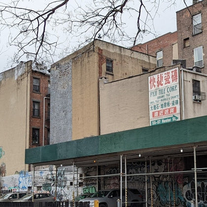 Urban scene with graffiti-covered walls, brick buildings, and a sign for a tile company on a beige structure under a green awning.