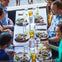 A group of six people sitting around a table sharing a meal with drinks, salads, and plates of food in an outdoor setting.