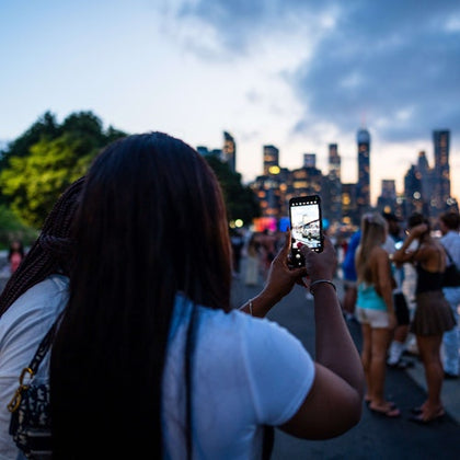 Person taking a photo of a city skyline with a crowd of people in the foreground during dusk.