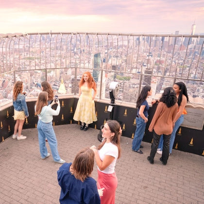 People enjoying the view from an observation deck at sunset, with a cityscape visible through the railing.