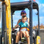 A woman and a child sitting inside a small excavator, with the child smiling and the woman operating the controls.